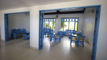 A dining area with blue chairs and tables, a bench, and a doorway leading to another room.