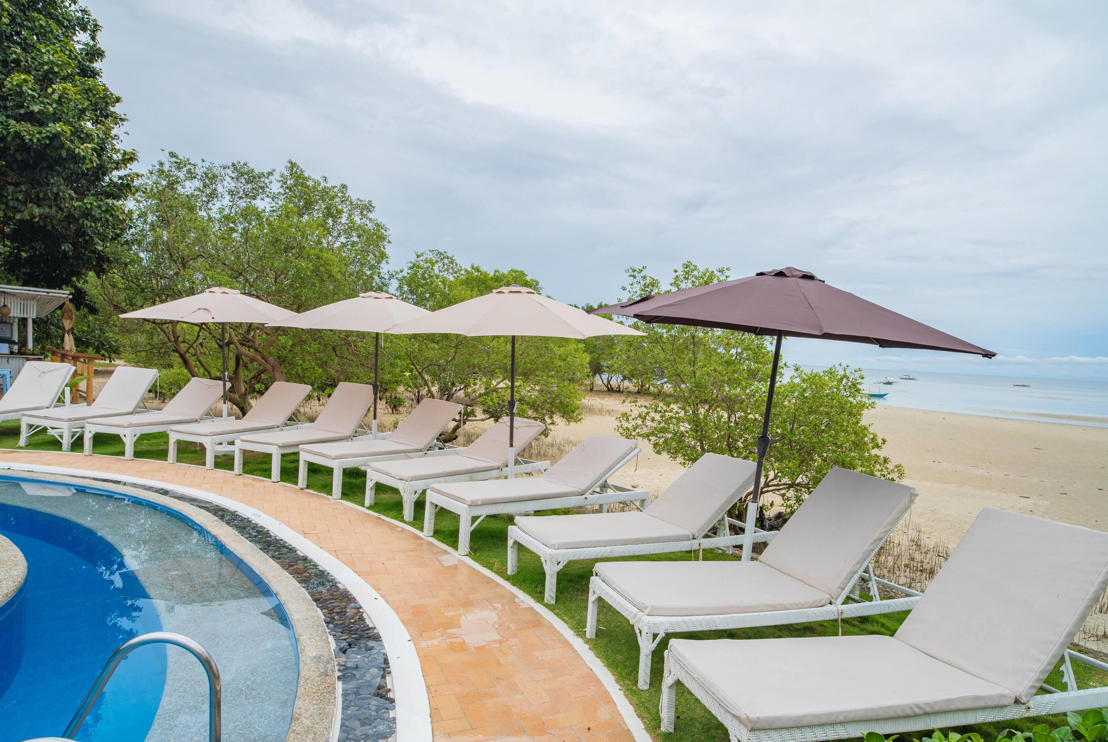 Un espace aménagé au bord de la piscine, avec des chaises longues et des parasols, un ciel dégagé et une vue sur la plage.