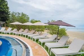 Un espace aménagé au bord de la piscine, avec des chaises longues et des parasols, un ciel dégagé et une vue sur la plage.