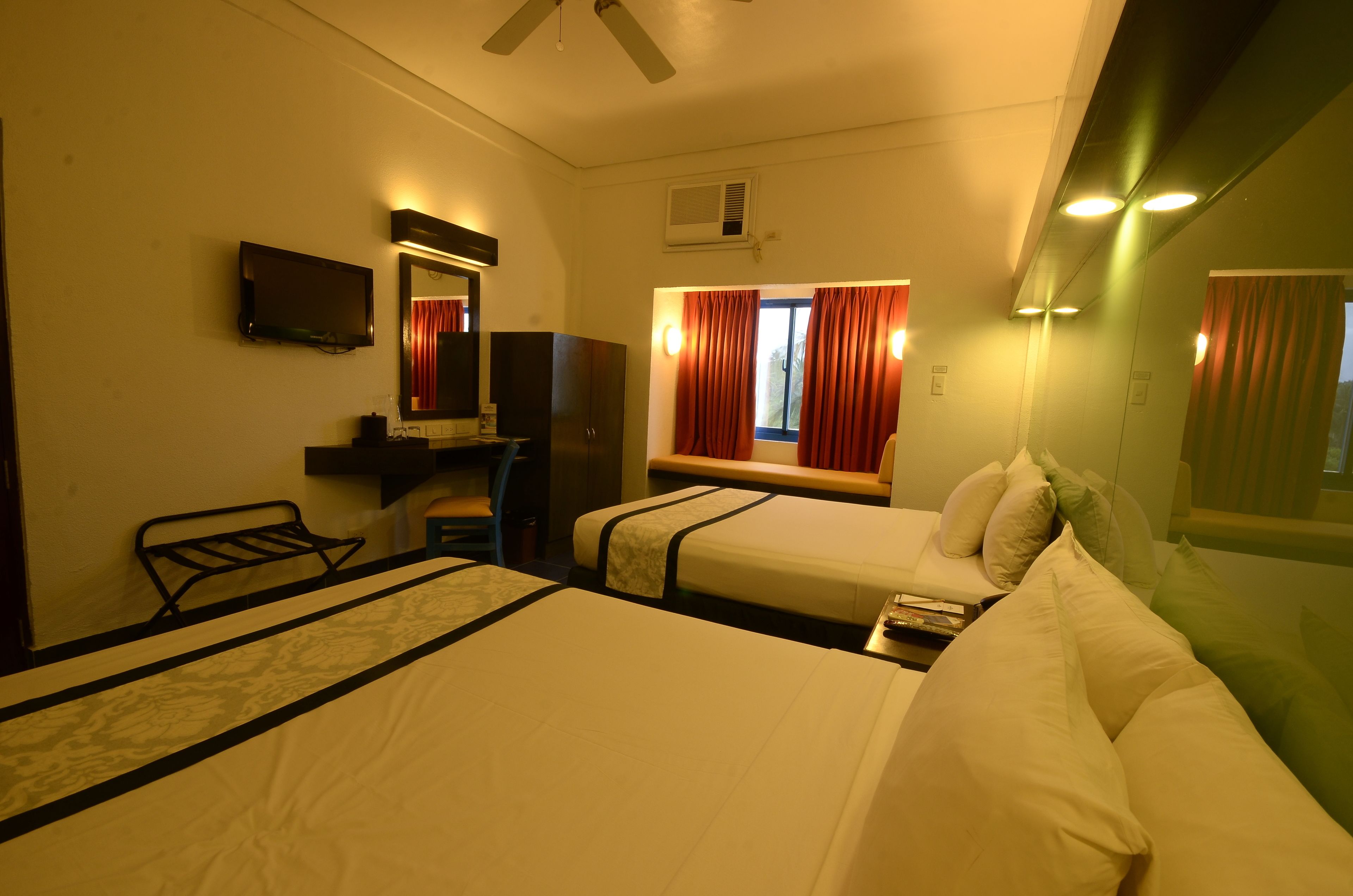 A hotel room with two beds, a TV, a desk, and a window with curtains.