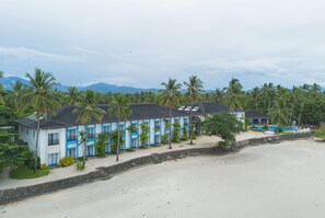 Un hôtel situé en bord de mer, doté de nombreuses chambres, d’une piscine et de palmiers.