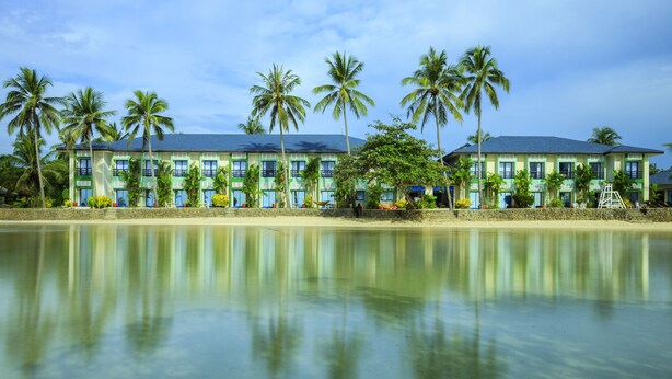 A beachfront hotel with multiple-story architecture, palm trees, and a clear view of the ocean.