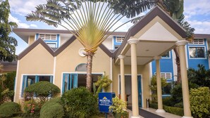 A hotel entrance with a sign, palm trees, and a covered walkway.
