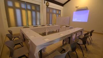 Una sala de conferencias con una larga mesa, sillas, una pantalla de proyector y una pizarra.