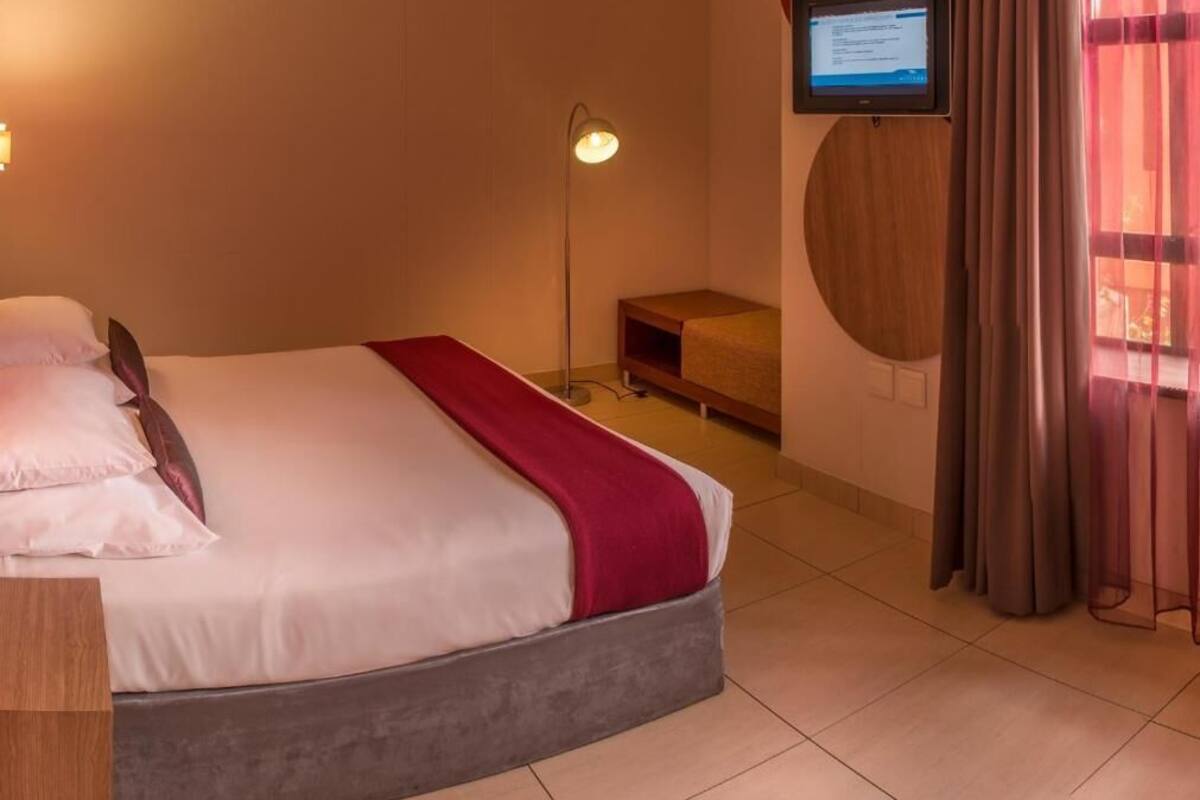 A hotel room with a bed, a desk, a television on the wall, and a floor lamp.
