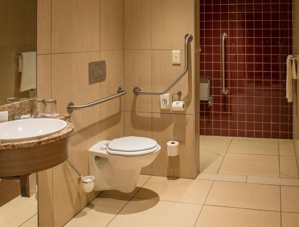 Een moderne badkamer met toilet, handgrepen, wastafel en spiegel.