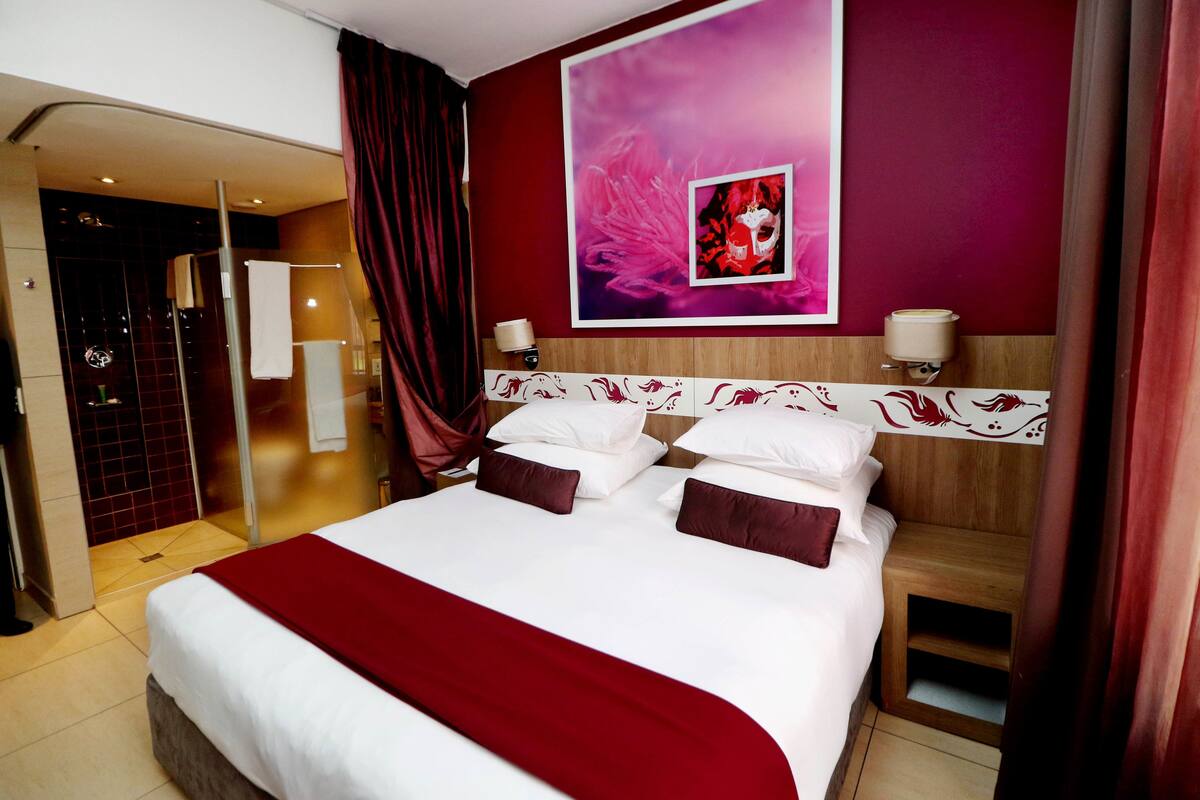 A hotel room with a large bed, a shower area, and a wall with a decorative painting.