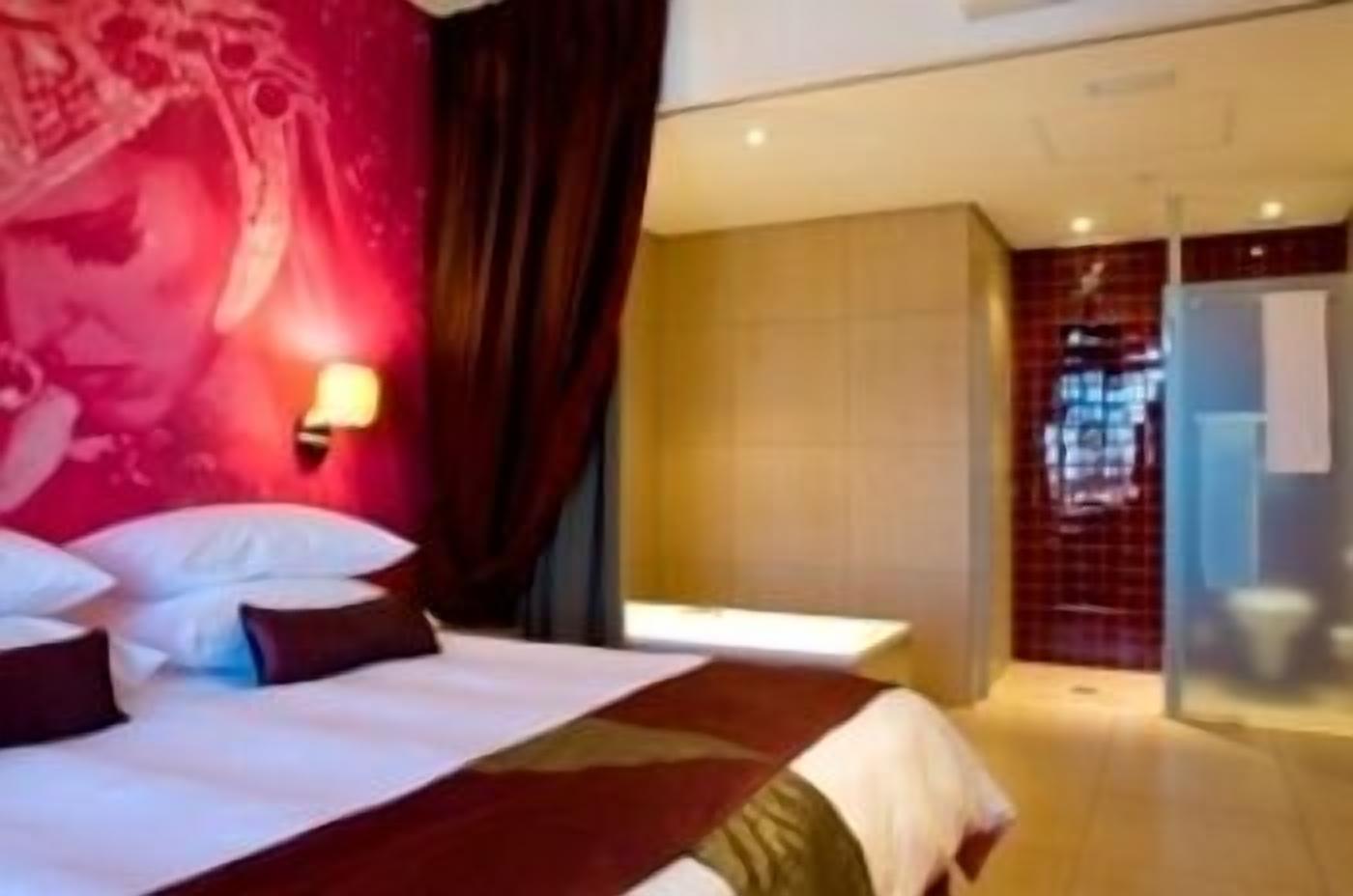 A hotel room with a large bed, a nightstand, a wall-mounted light, and a view of the bathroom.