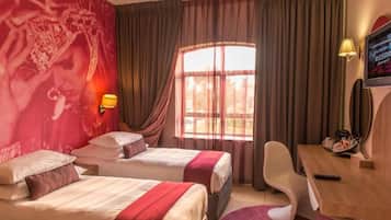 Quarto de hotel com duas camas, uma escrivaninha, uma cadeira, uma televisão e uma janela com cortinas.