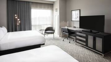 A hotel room with two beds, a desk, a television, and a chair.