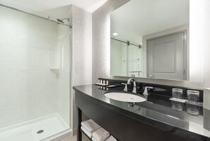 A modern bathroom with a glass-enclosed shower, a black countertop, and a large mirror.