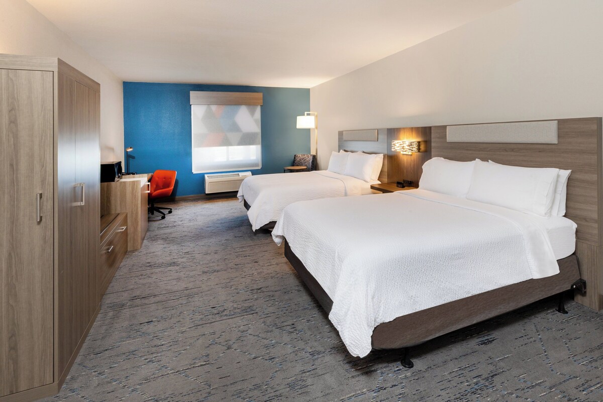 A hotel room with two beds, a desk, a chair, and a large window.