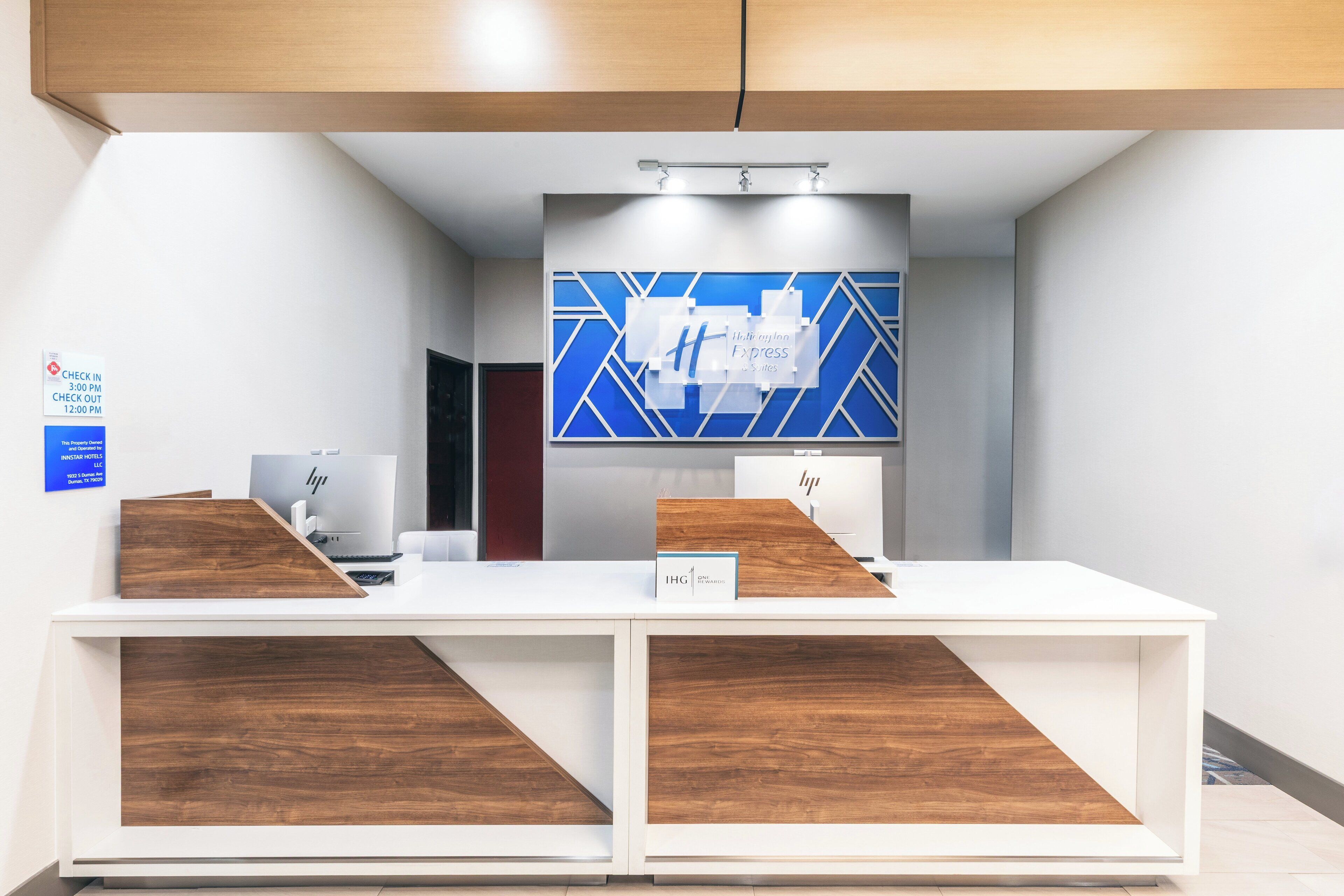 A reception desk with a modern design, featuring a check-in/check-out sign, a digital display, and a wooden accent.