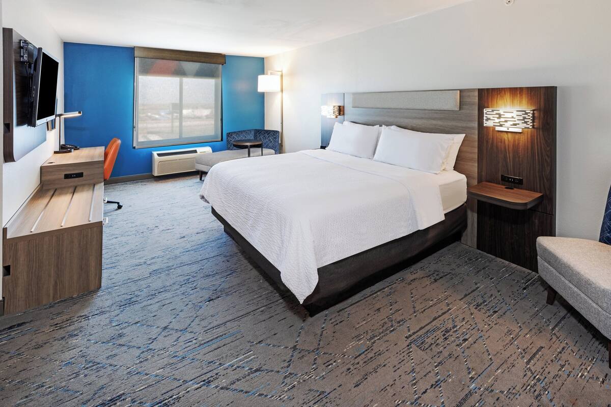 A hotel room with a large bed, a desk with a chair, a TV, and a window with a view.