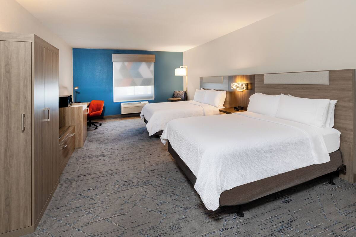 A hotel room with two beds, a desk, a chair, and a large window.