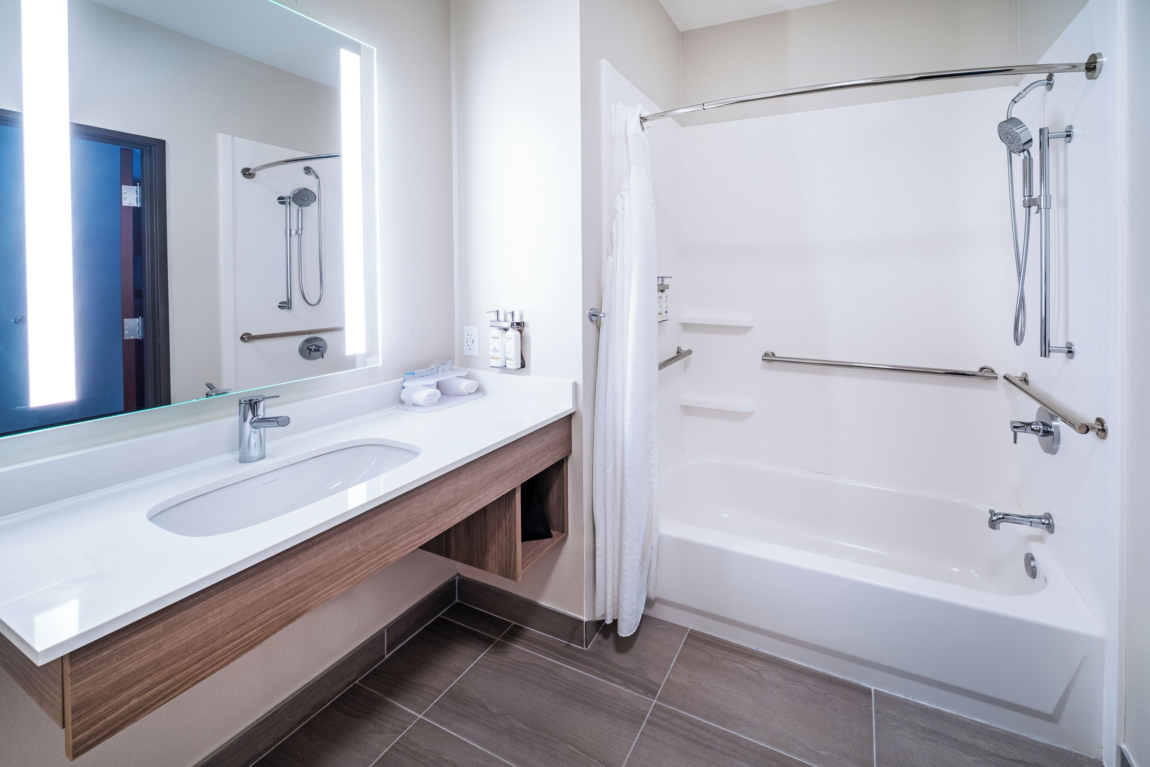 A modern bathroom with a large mirror, two sinks, a bathtub, and a shower.