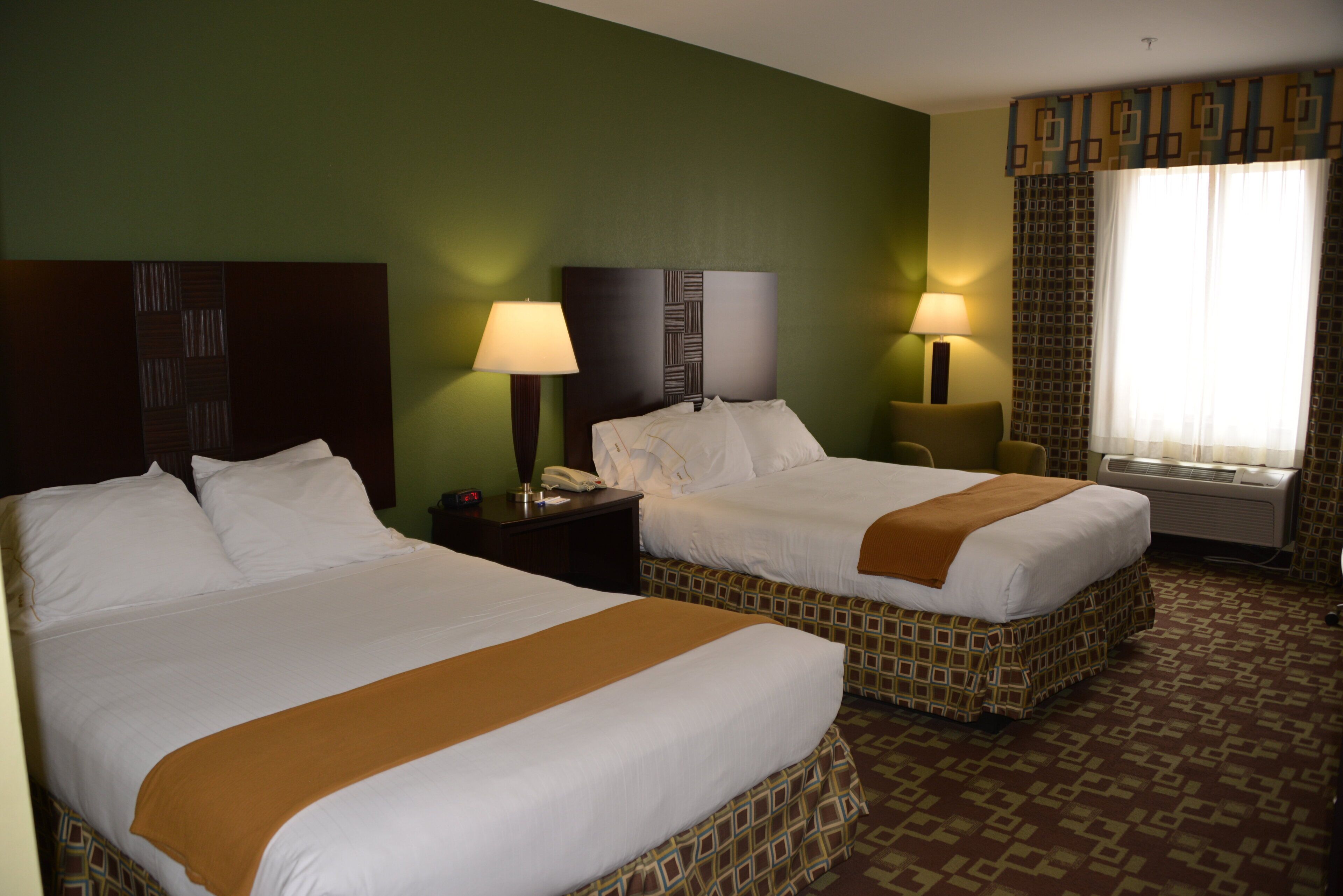 A hotel room with two beds, a nightstand with a lamp, a telephone, and a window with curtains.