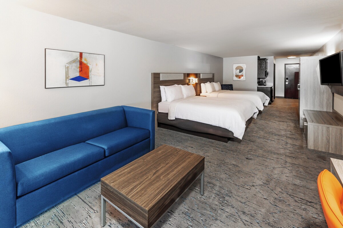 A hotel room with a large bed, a blue sofa, a wooden coffee table, and a TV.