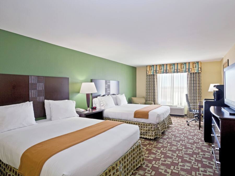 Habitación de hotel con dos camas, un escritorio, televisor y ventana con cortinas.