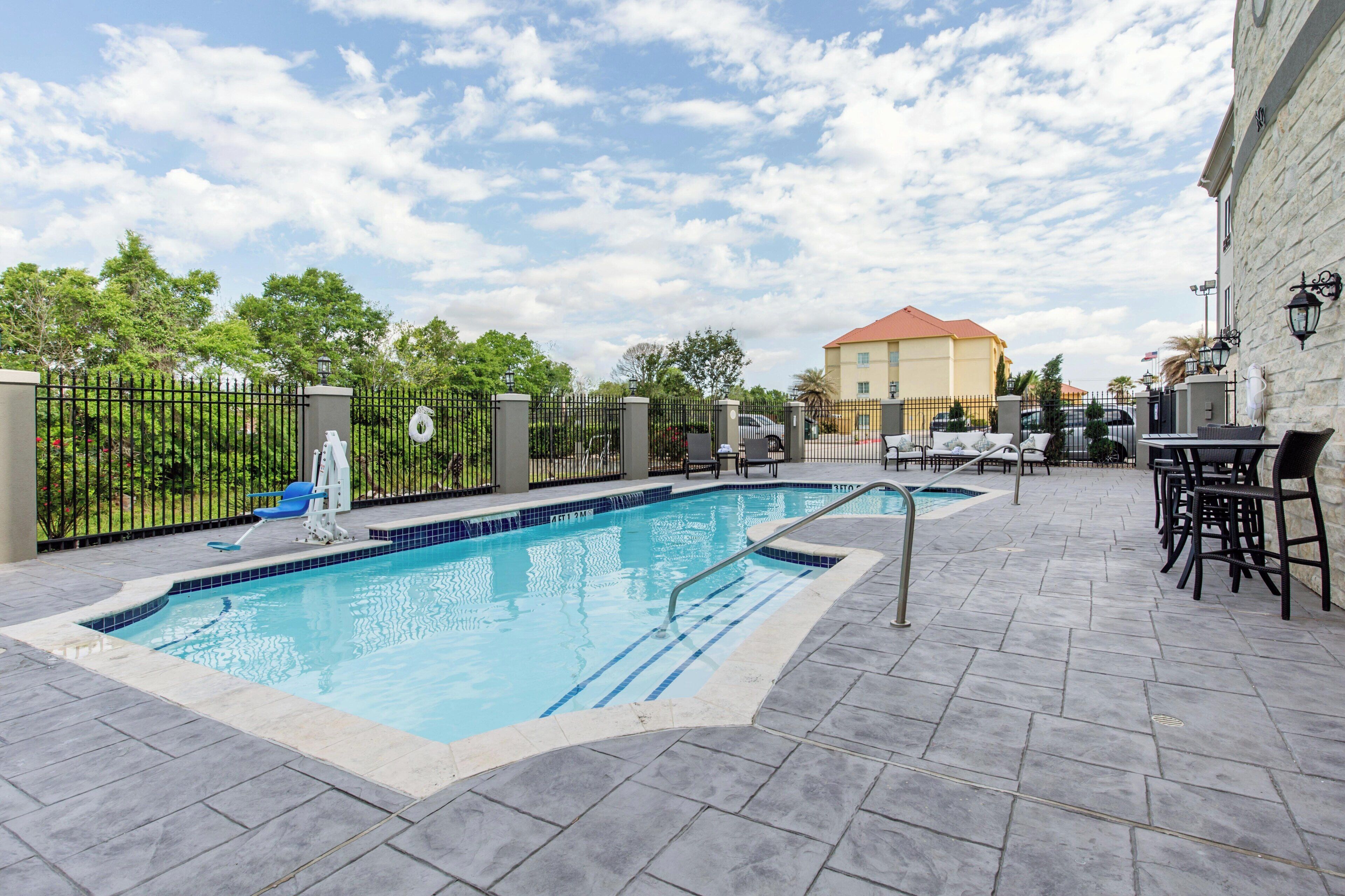 Piscina com deck ladrilhado, espreguiçadeiras e um edifício ao fundo.