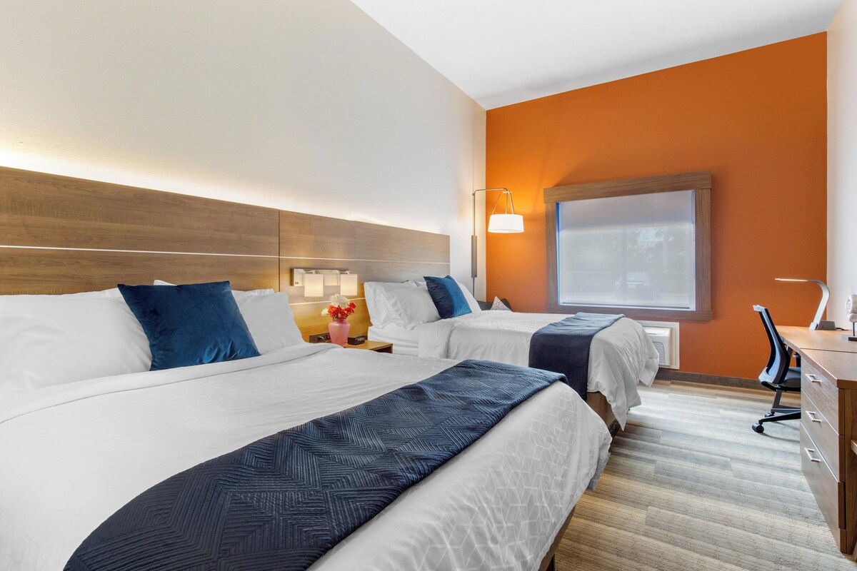 A hotel room with two beds, a desk, a chair, and a large window.