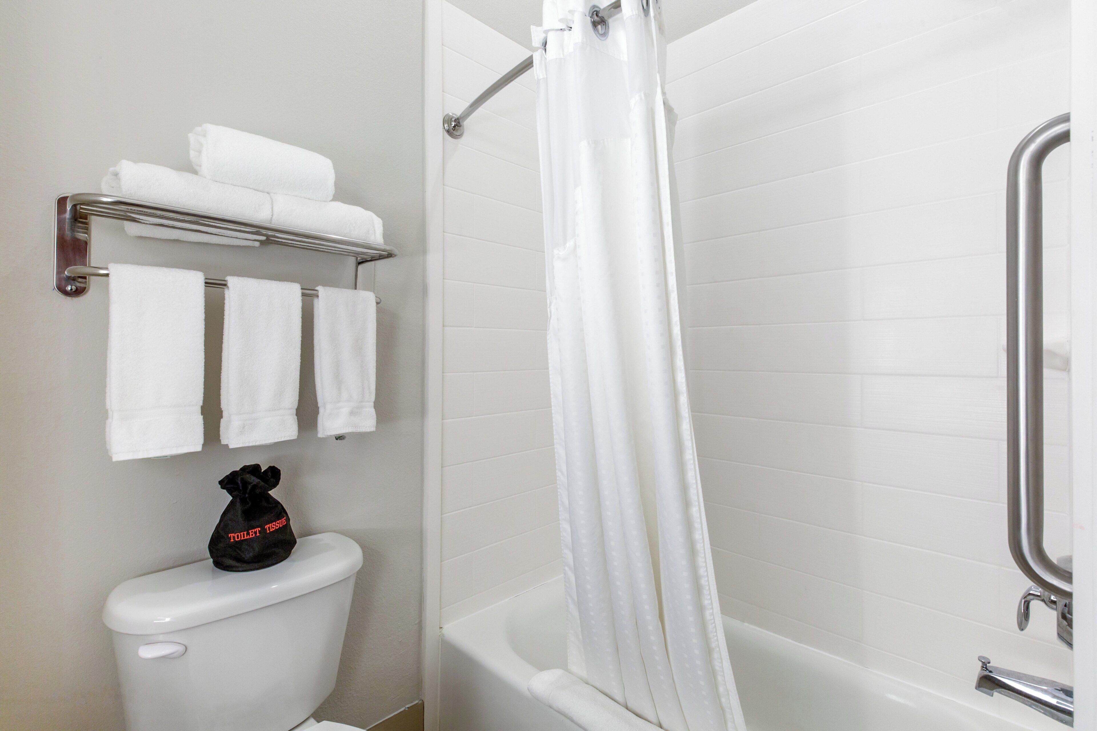 Une salle de bain comprenant des toilettes, une douche avec un rideau et un porte-serviettes avec des serviettes pliées.