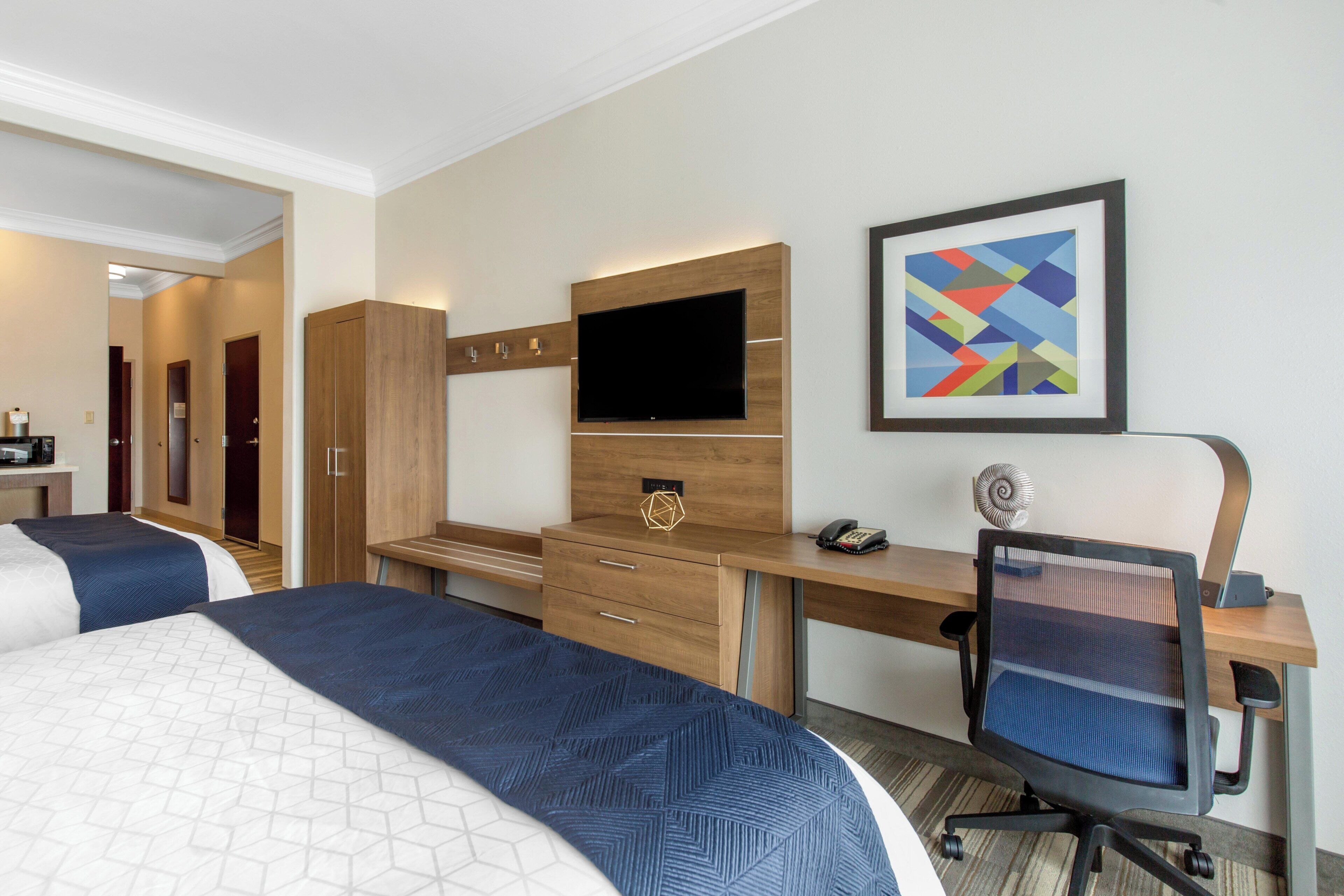 A hotel room with two beds, a desk, a chair, a television, and a framed artwork on the wall.