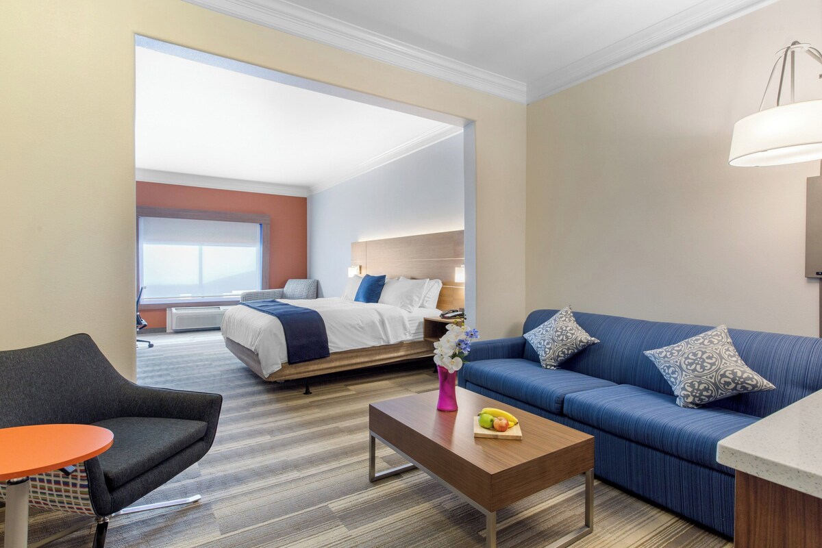 A hotel room with a bed, a sofa, a coffee table, and a chair.