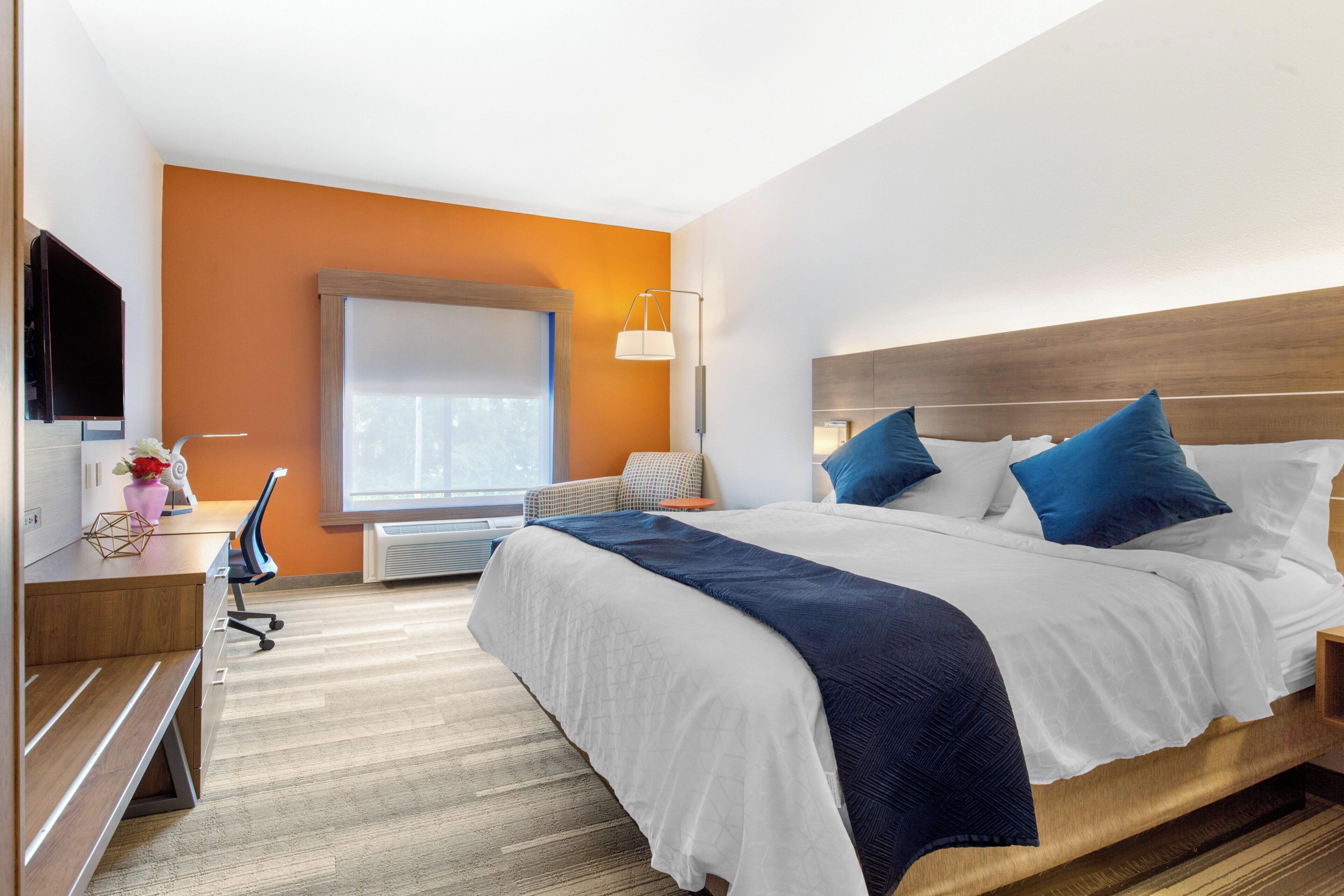 Habitación de hotel con una cama grande, un escritorio, una silla, un televisor, una ventana y una lámpara.