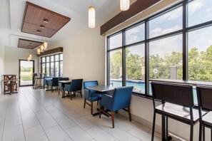 A spacious indoor area with multiple tables and chairs, large windows offering a view of the outdoors, and a ceiling with hanging lights. - Holiday Inn Express Hotel & Suites Houston-Alvin by IHG (Alvin)