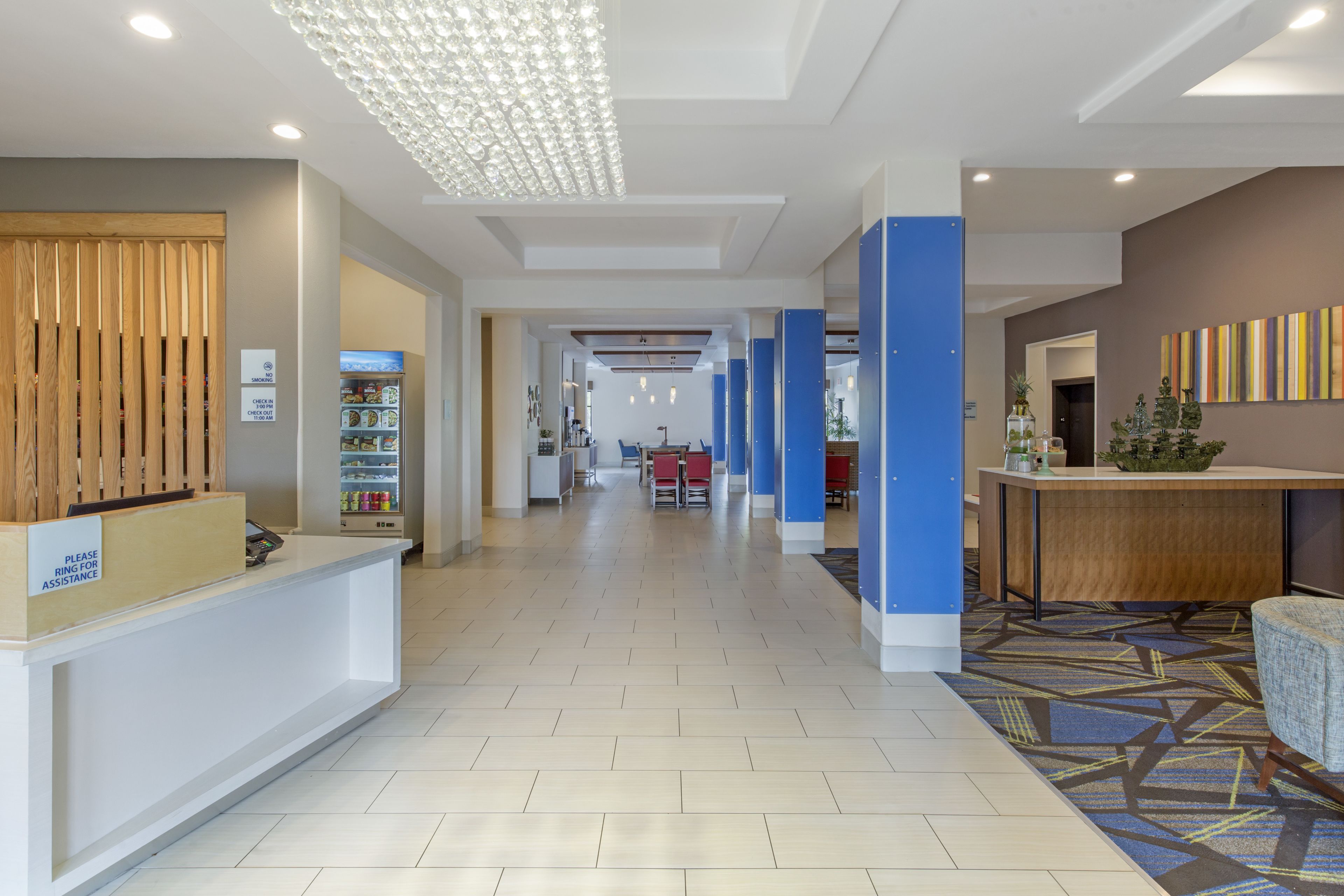Un'area di accoglienza hotel dal design moderno, con una reception, un'area d'attesa con sedute e una lampada decorativa a soffitto.