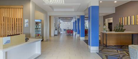 A hotel reception area with a modern design, including a reception desk, a waiting area with chairs, and a decorative ceiling light.