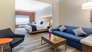 A hotel room with a bed, a blue sofa, a small table with fruit, and a chair.