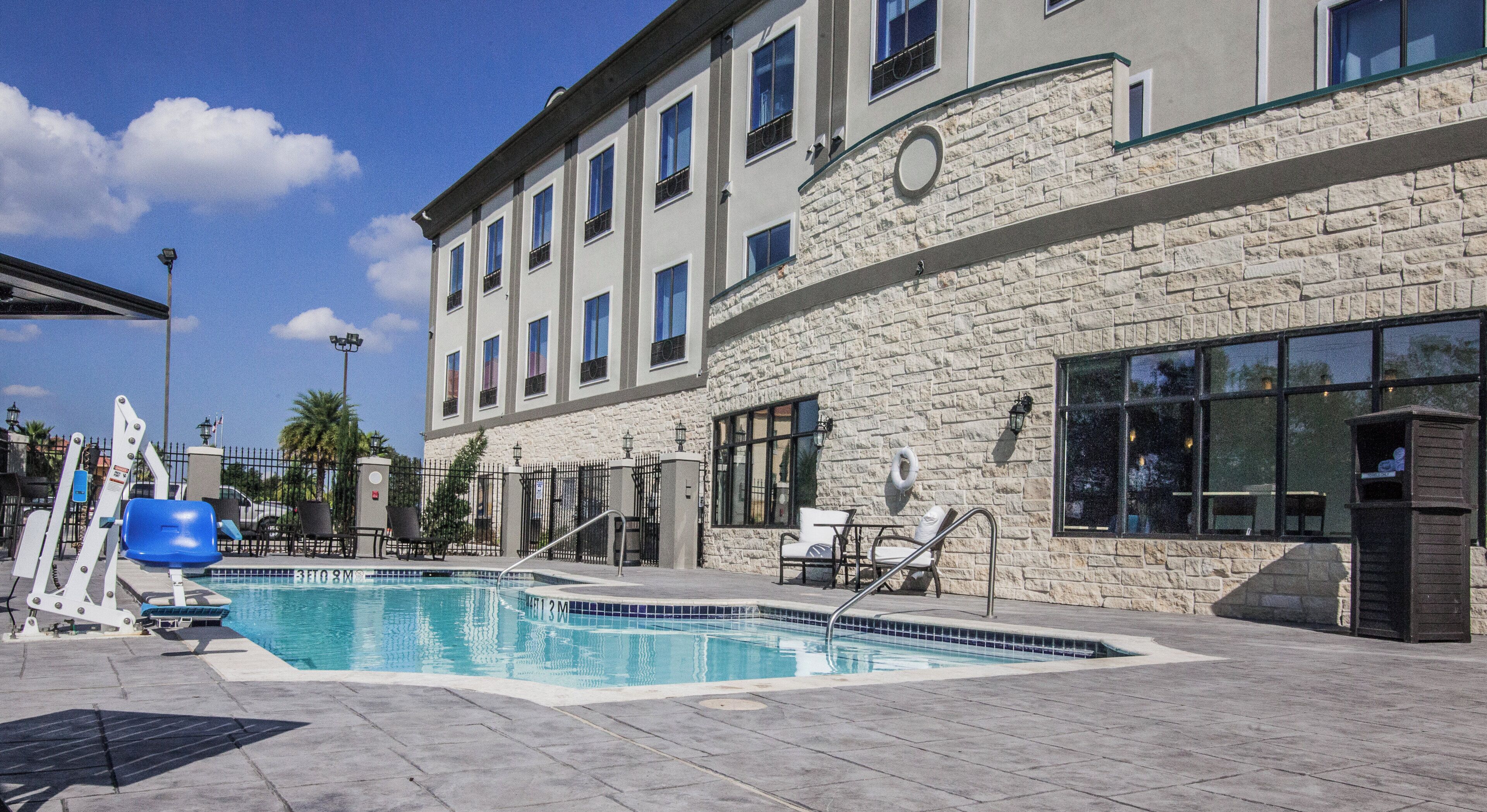Un espace piscine avec des chaises longues et un bâtiment en pierre doté de nombreuses fenêtres.