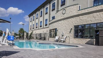 Un espace piscine avec des chaises longues et un bâtiment en pierre doté de nombreuses fenêtres.