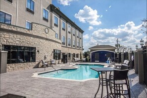 A hotel with a swimming pool, outdoor seating, and a stone facade.