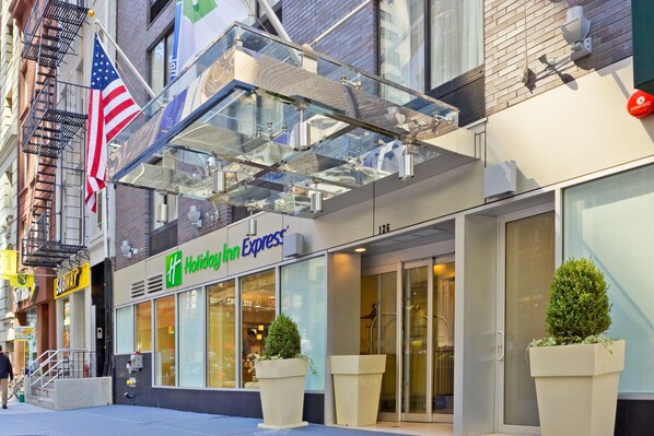 A Holiday Inn Express hotel with a glass entrance, American flag, and a Subway sandwich shop across the street. - Holiday Inn Express New York City- Wall Street by IHG (New York)