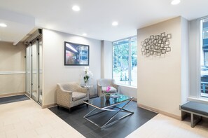 Un espace d’attente moderne, comprenant deux fauteuils à motifs, une table basse en verre et un élément décoratif mural.