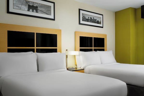 A hotel room with two beds, a nightstand with a lamp, and two framed pictures on the wall.
