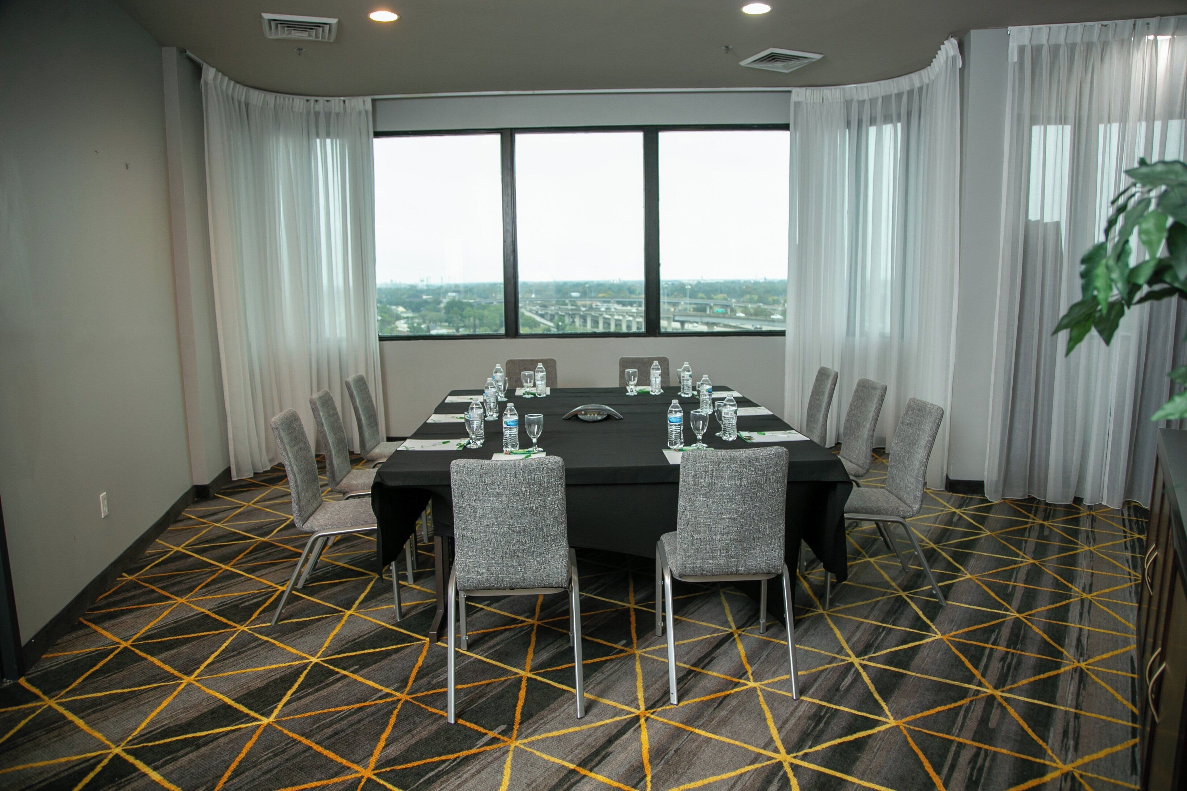 A conference room with a large table, chairs, and a view through large windows.