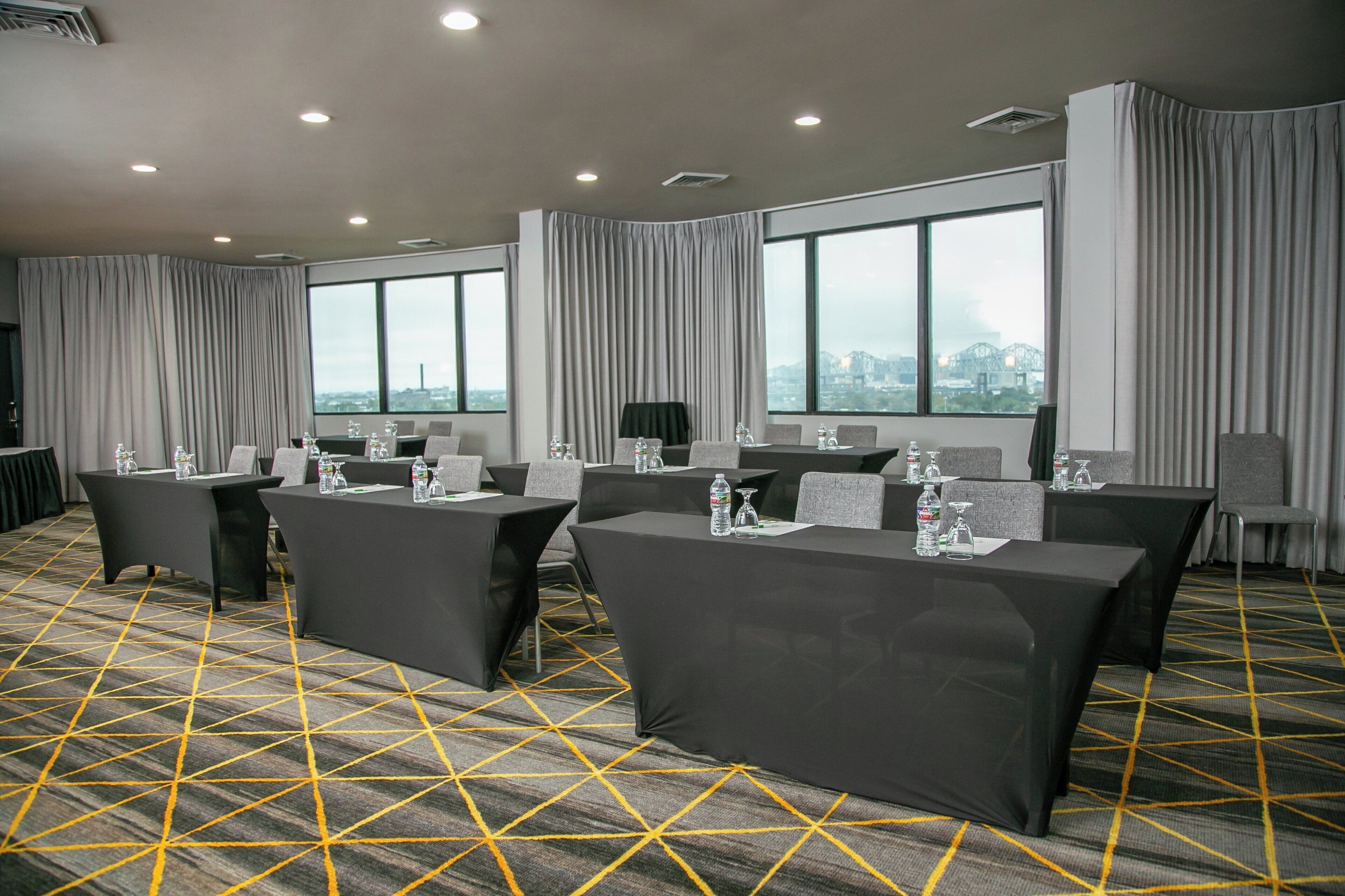 A conference room with tables, chairs, and large windows with curtains.