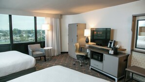 A hotel room with two beds, a desk with a TV, a chair, a small table, and a view of the city. - Holiday Inn New Orleans West Bank Tower by IHG (Gretna)