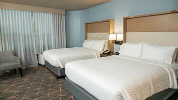 A hotel room with two beds, a chair, a nightstand with a lamp, and a window with curtains.