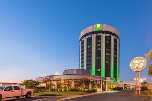 A hotel with a prominent sign for a bar and grill, a parking lot with vehicles, and a clear sky. - Holiday Inn New Orleans West Bank Tower by IHG (Gretna)