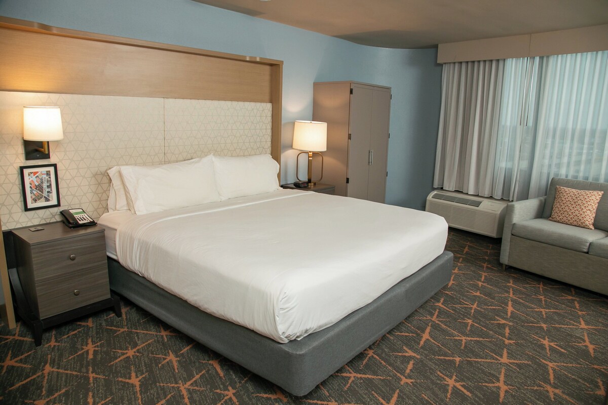 Een hotelkamer met een groot bed, twee nachtkastjes met lampen, een kledingkast, een sofa en een kamerbreed tapijt met een patroon.