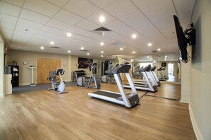 Un gimnasio con cintas de correr, elípticas y un espejo grande.
