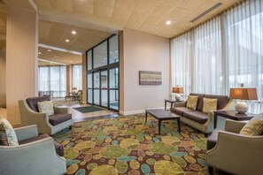 Vestíbulo de hotel con un amplio ventanal, una recepción y una zona de estar con sofás y sillones.