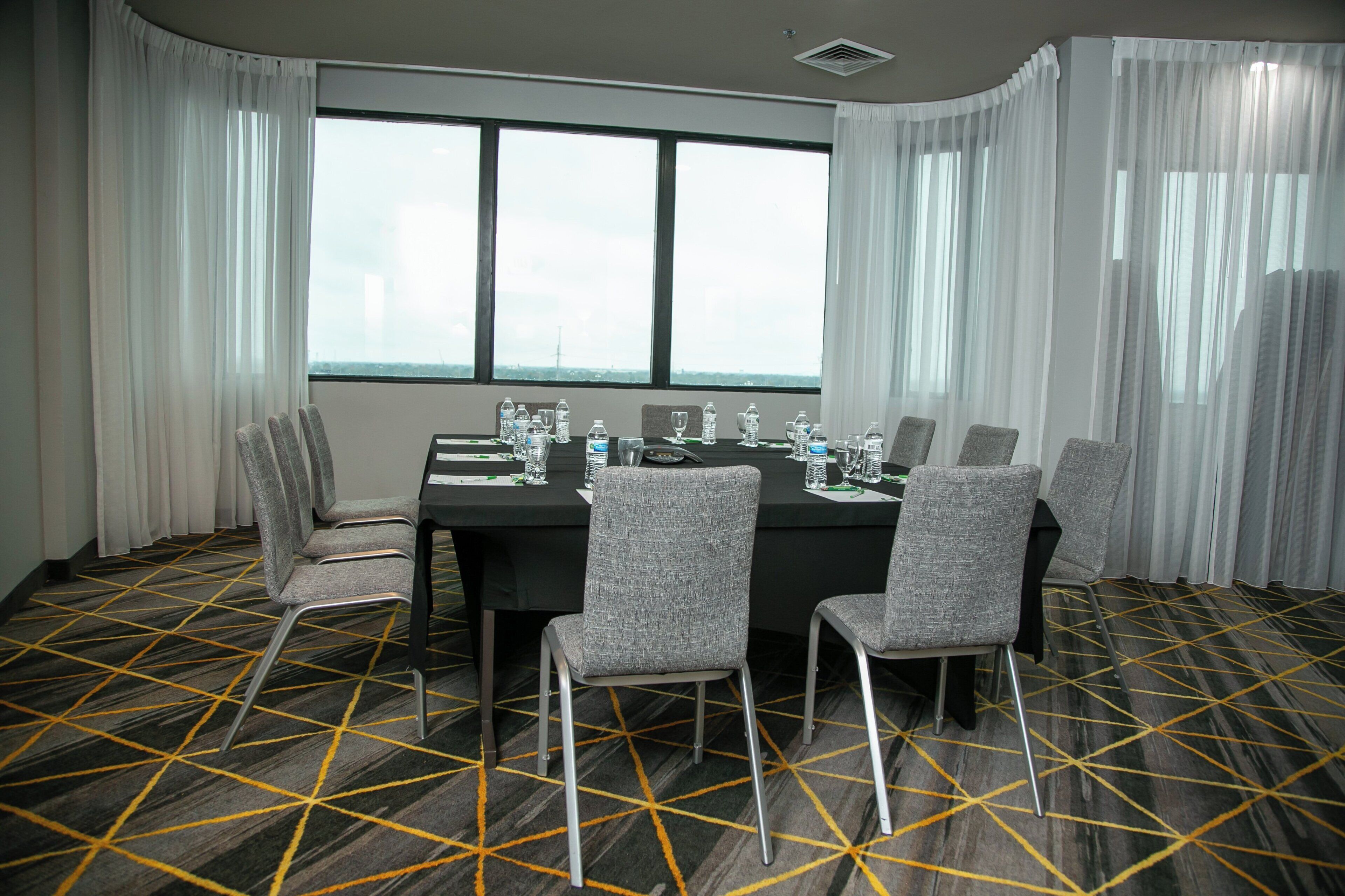 Ein Konferenzraum mit einem großen Tisch, sechs Stühlen und Blick durch hohe Fenster.