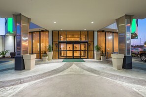A hotel entrance with a glass door, potted plants, and a tiled pathway leading to the entrance. - Holiday Inn New Orleans West Bank Tower by IHG (Gretna)
