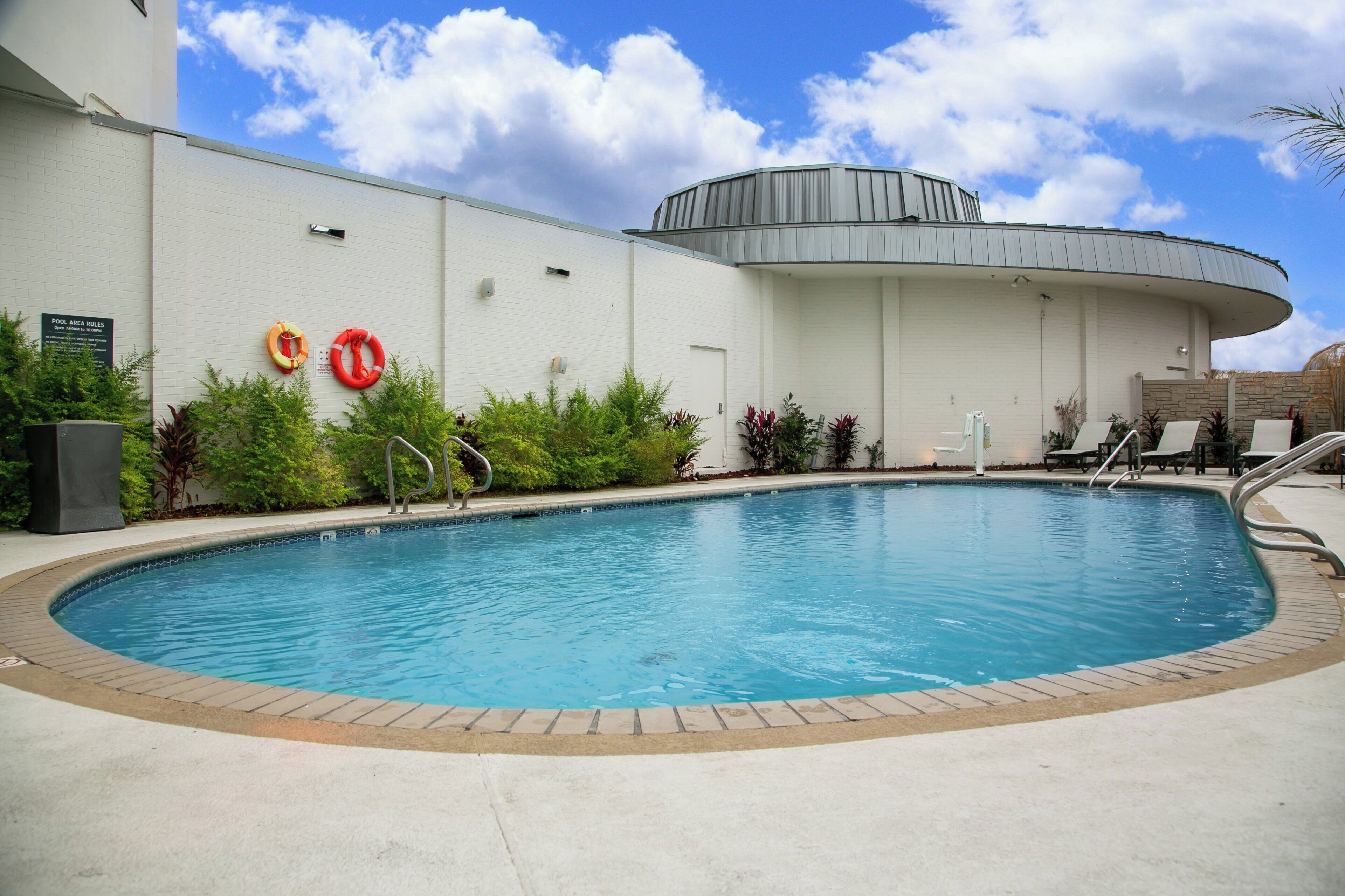 A swimming pool with a curved edge, surrounded by a white wall with a sign indicating pool area rules.